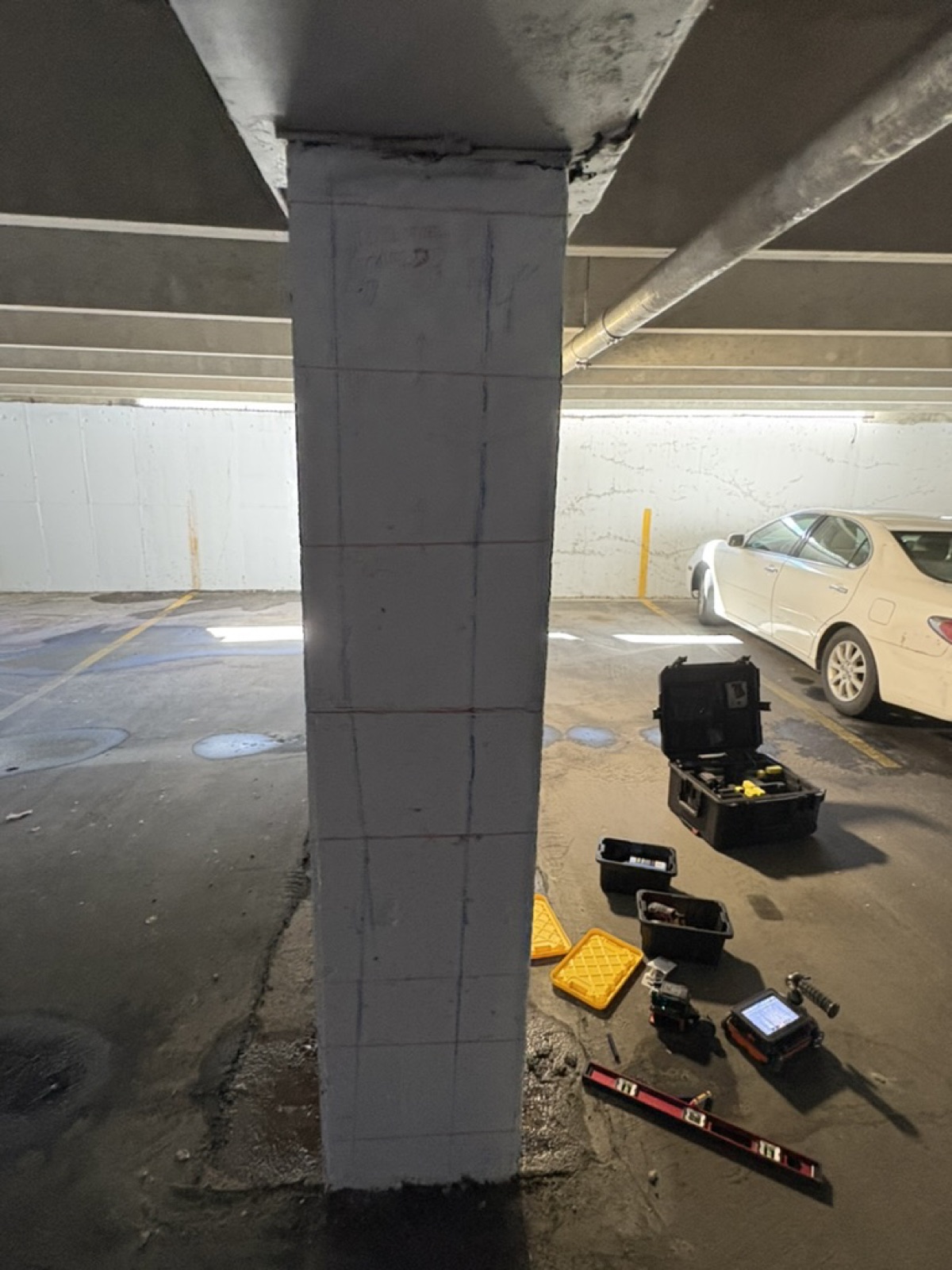 Free-standing concrete column gridded on all visible faces, with scanning kit and cases spread on the deck behind it