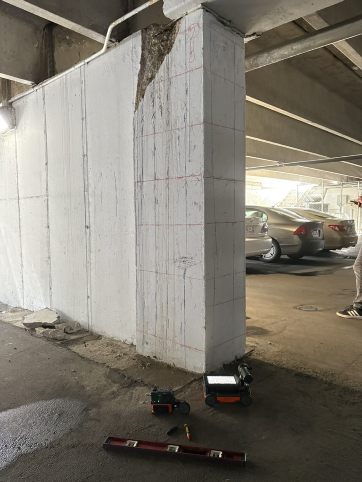 End of a concrete shear wall in a parking garage, gridded in blue and red layout lines, with two GSSI FLEX NX radar units and a level on the floor at its base